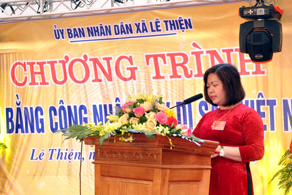 A person standing at a podium with flowers in front of a signDescription automatically generated with medium confidence