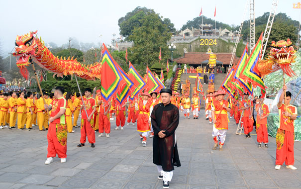A group of people in traditional attire walking with flagsDescription automatically generated