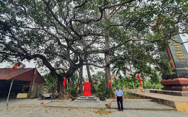 A person sweeping a stone with a red object under a treeDescription automatically generated