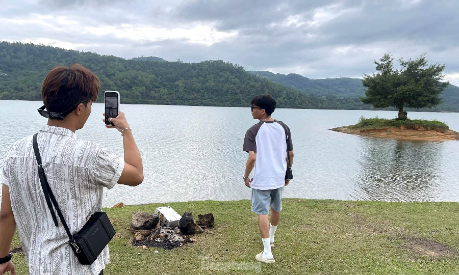 A person taking a picture of another person by a lakeDescription automatically generated