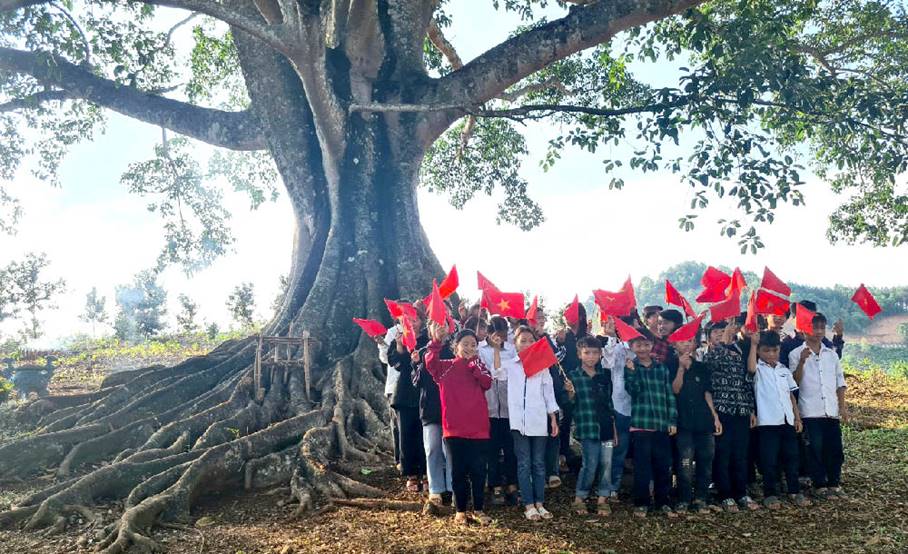 A group of people holding flags under a treeDescription automatically generated