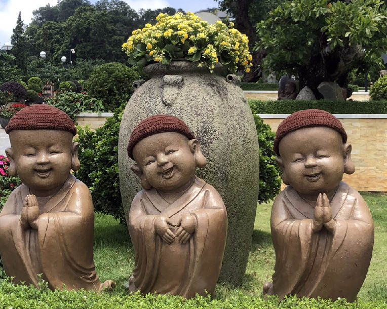 Statues of smiling children in a garden with Leshan Giant Buddha in the backgroundDescription automatically generated